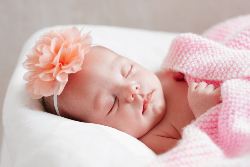 Bébé à gilet rose et serre-tête à fleur qui dort